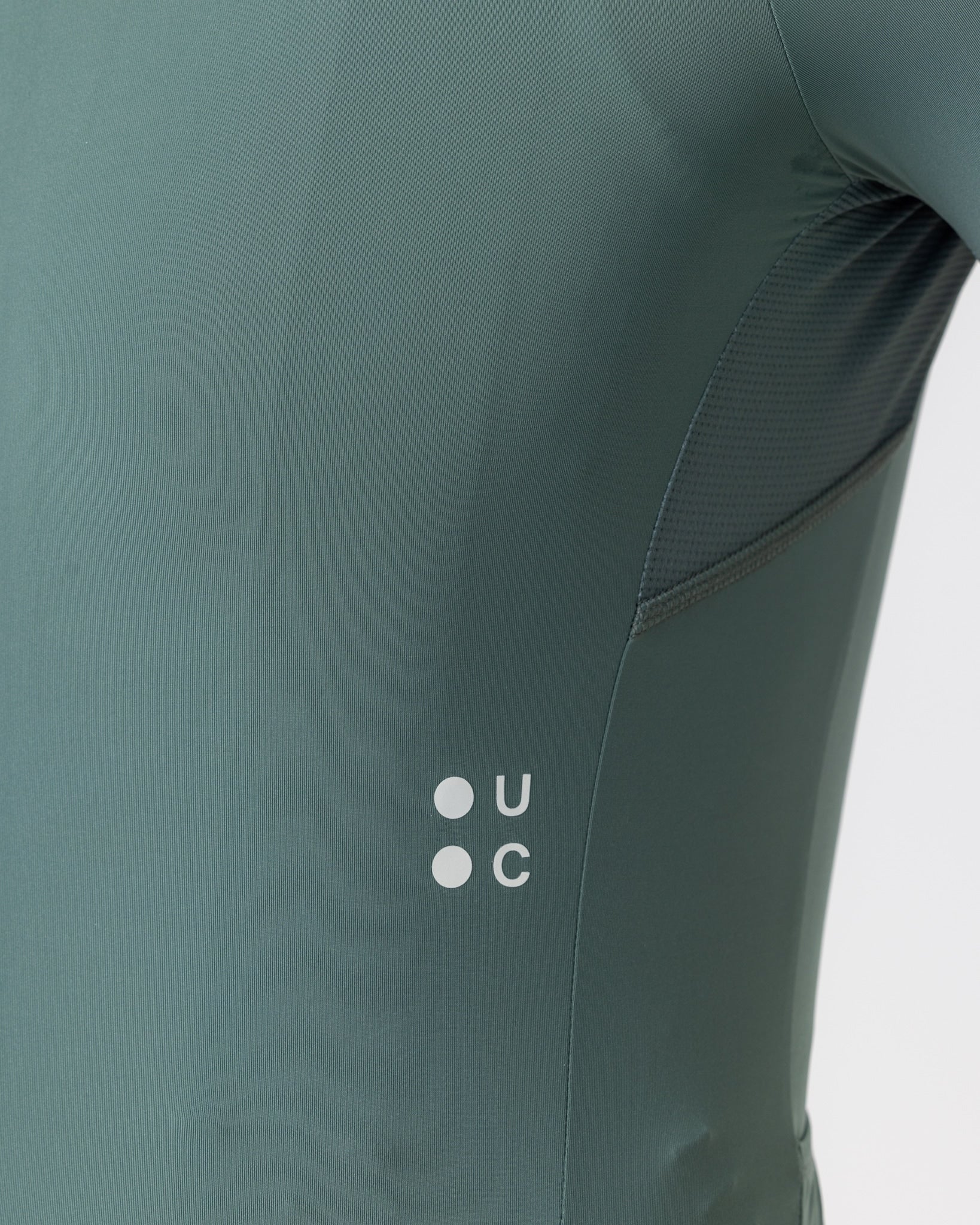 Side detail: white UC dot logo and mesh underarm ventilation panel on the Men's Mono Short Sleeve Jersey in Green Daze.