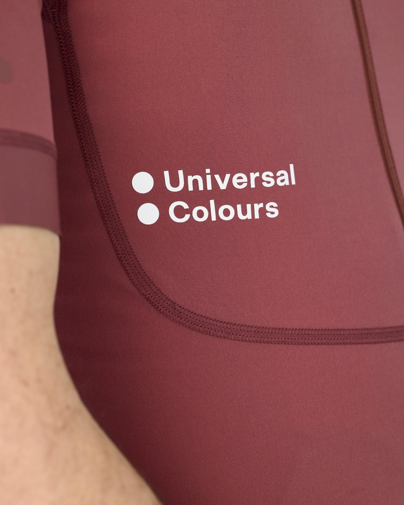 Close-up of the white Universal Colours chest logo and curved front-pocket stitching on the Jaipur Red Chroma jersey.