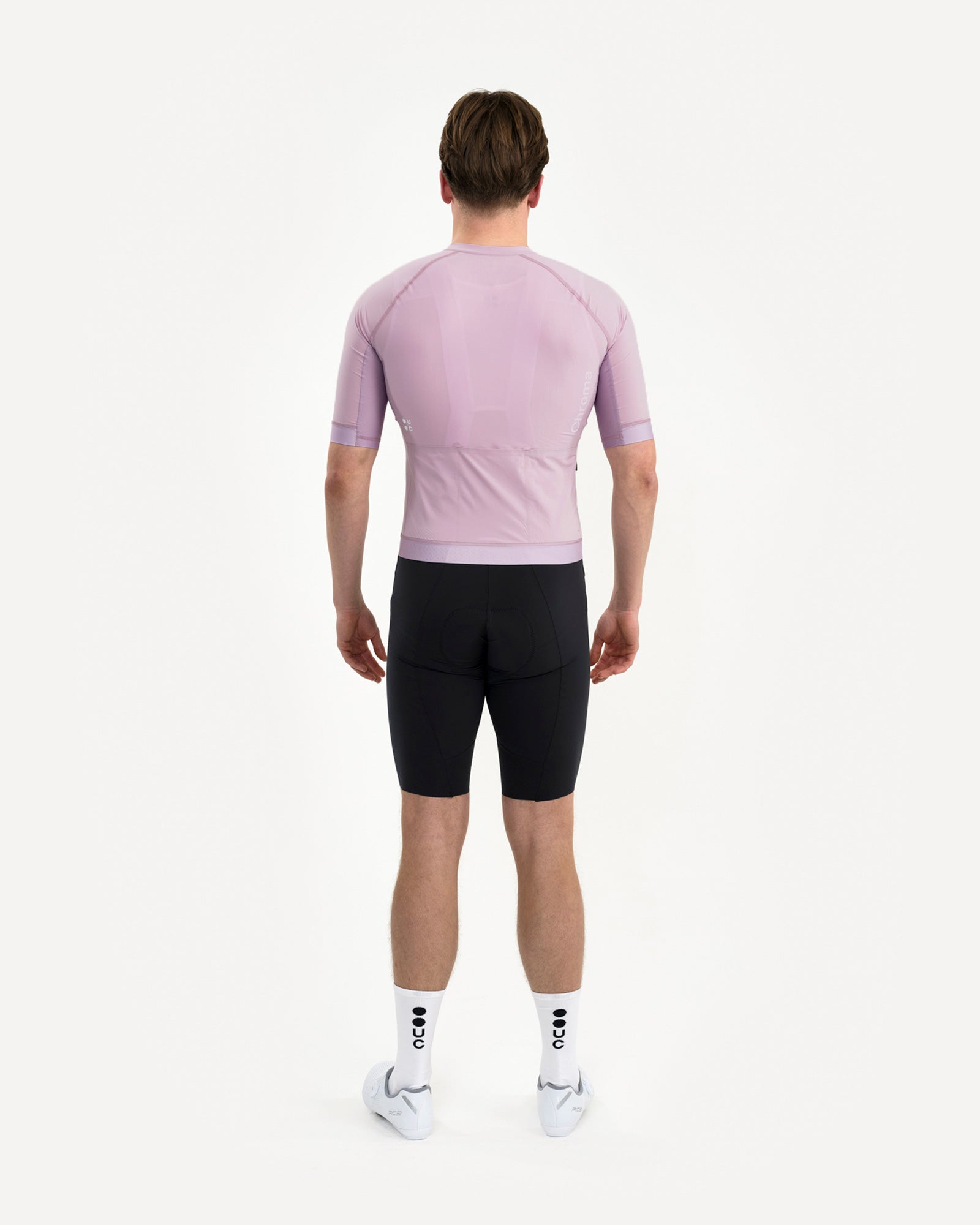 Back view of the Men's Chroma Short Sleeve Jersey in Washed Lilac, worn with black bib shorts and white UC socks.