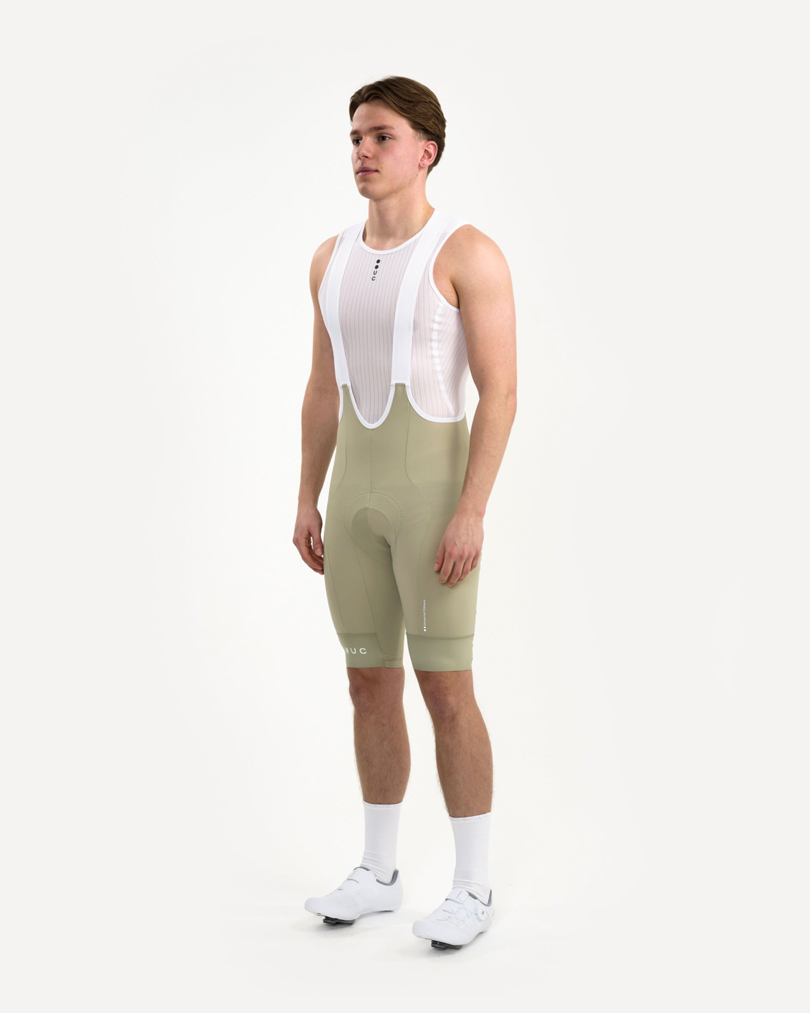 Three-quarter front view of the Men's Mono Bib Shorts 2.0 in Green Tea, paired with a white UC mesh base layer and socks.