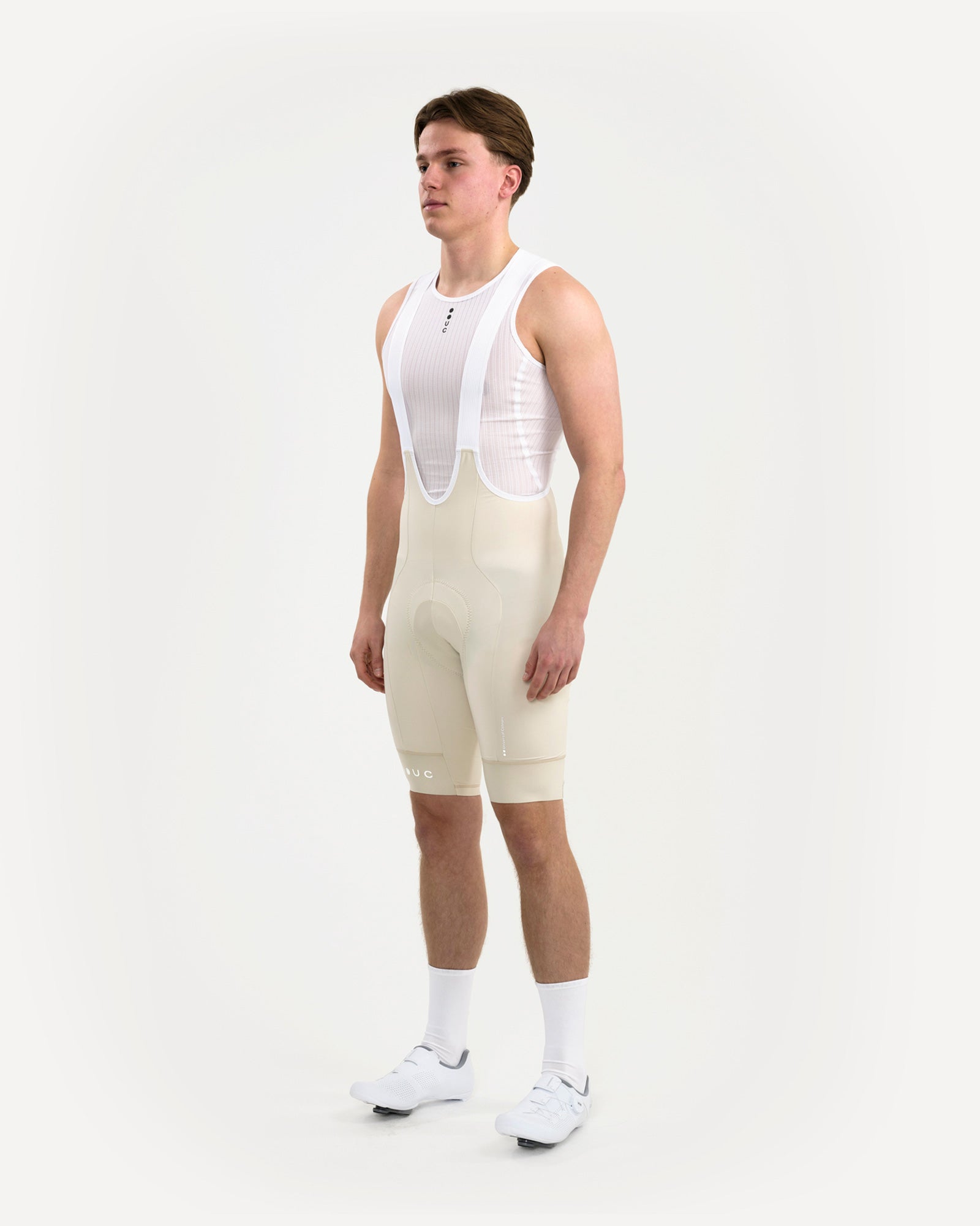 Three-quarter view of the Men's Mono Bib Shorts 2.0 in Off White, paired with a white UC mesh base layer.