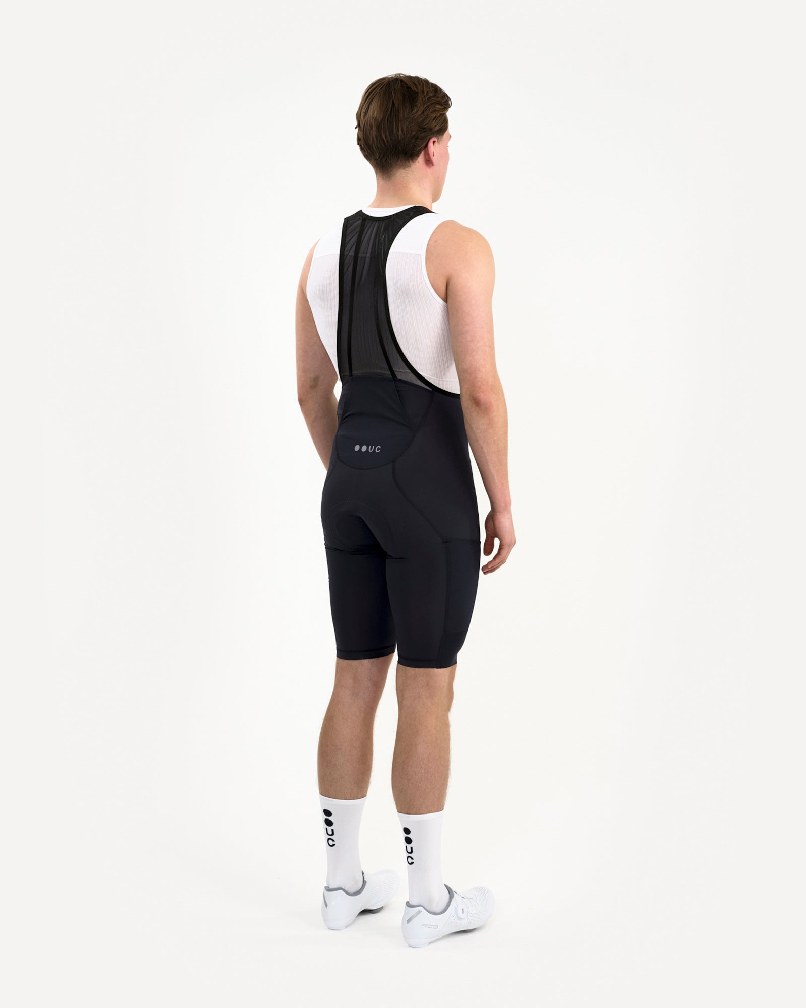 Three-quarter back view of the Men's Mono Cargo Bib Shorts in Navy Blue on model, showing tonal UC dot-logo on the rear yoke.