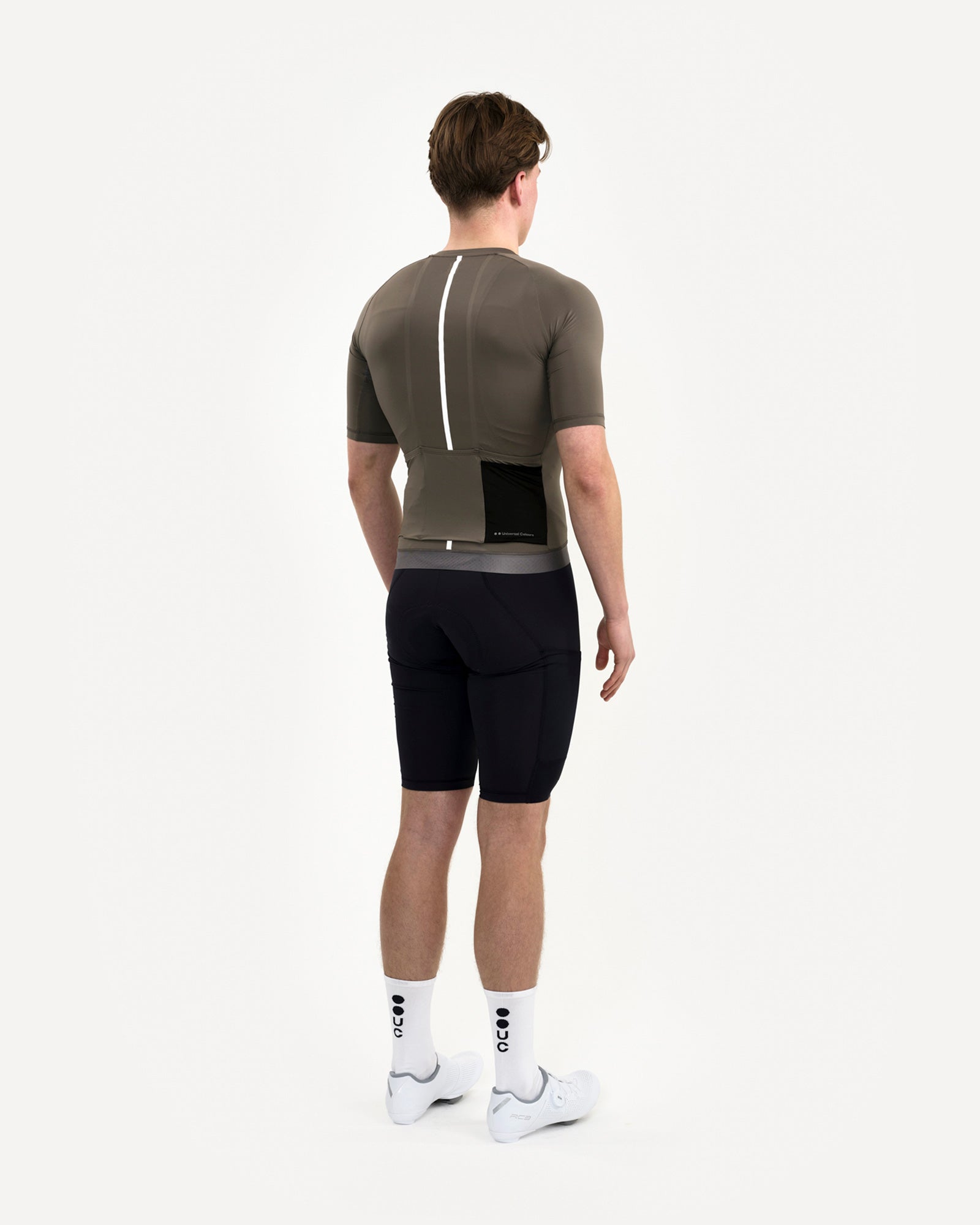 Model in the Men's Mono Short Sleeve Jersey in Soft Grey, back view, paired with black bib shorts and white UC socks.
