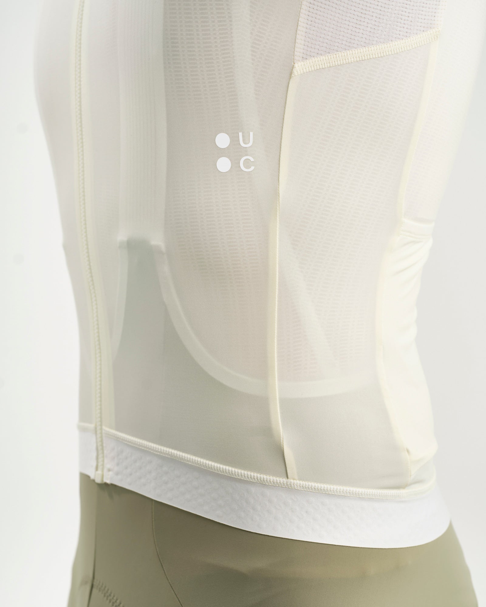 Close-up of the tonal UC dot logo on the Tampered White jersey, with sheer ventilation panel and honeycomb gripper hem.