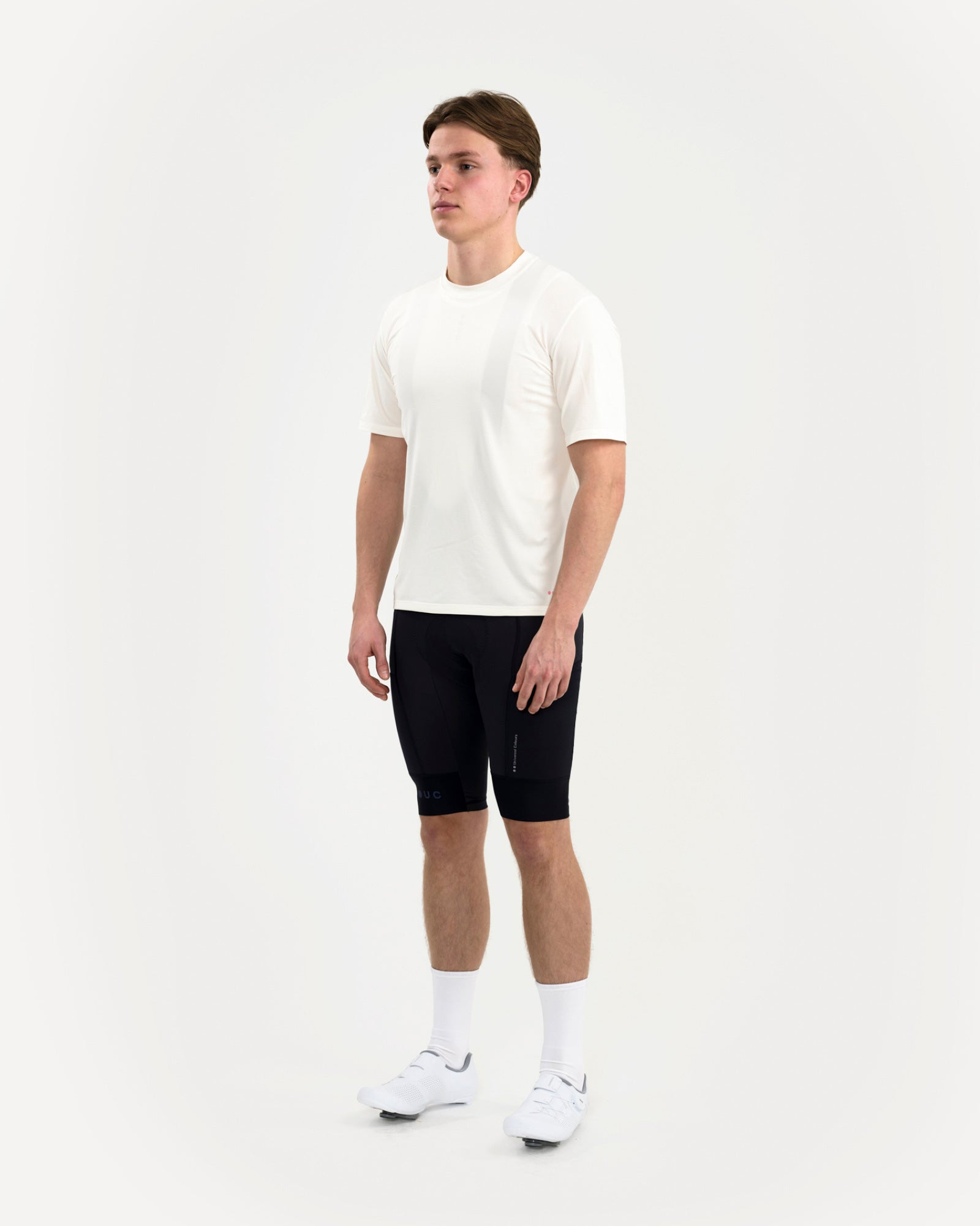Three-quarter front view: man in the Universal Colours Tech Tee in Off White with black cycling bib shorts.