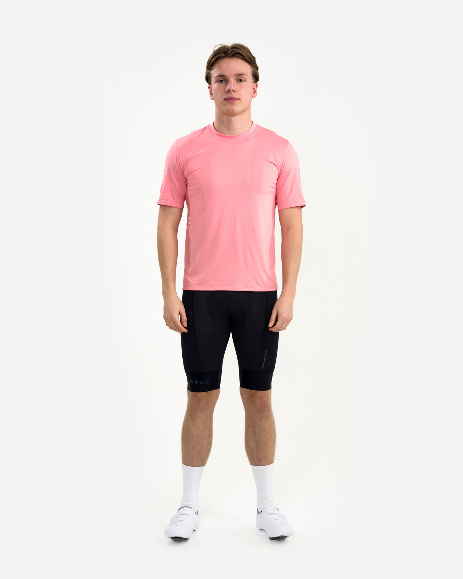 Male model front view in the Tech Tee in Washed Pink with black UC bib shorts, white socks and cycling shoes.