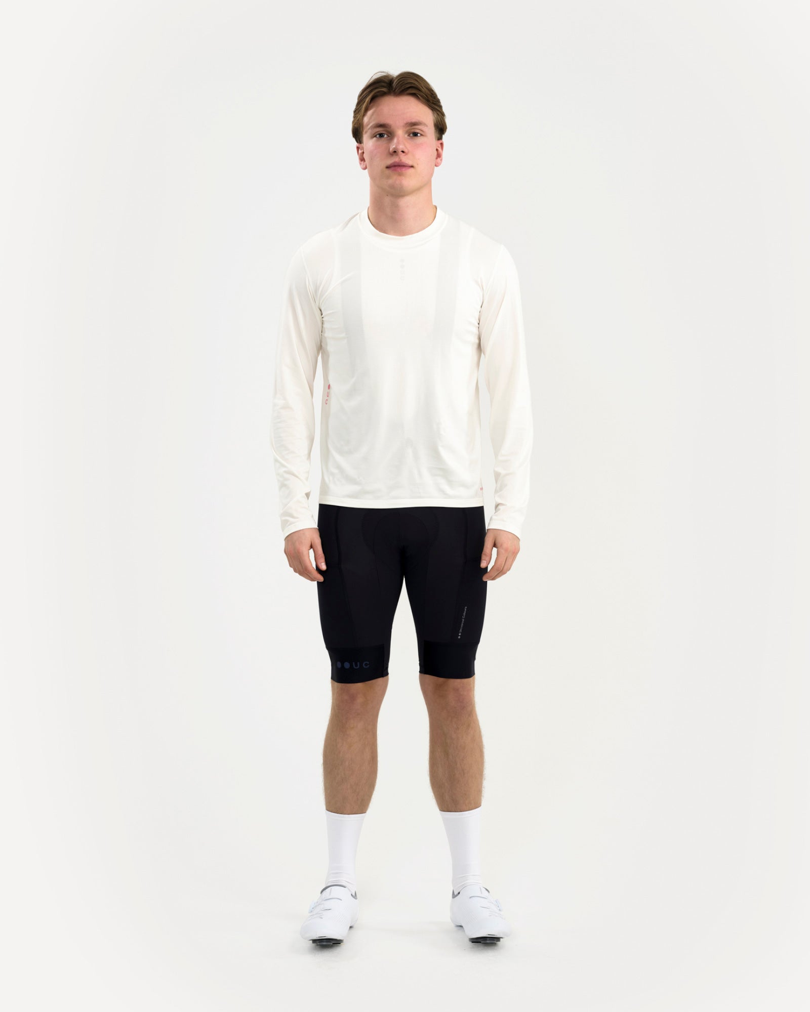 Male model wearing the Long Sleeve Tech Tee in Off White, front view, paired with UC black cycling bib shorts.