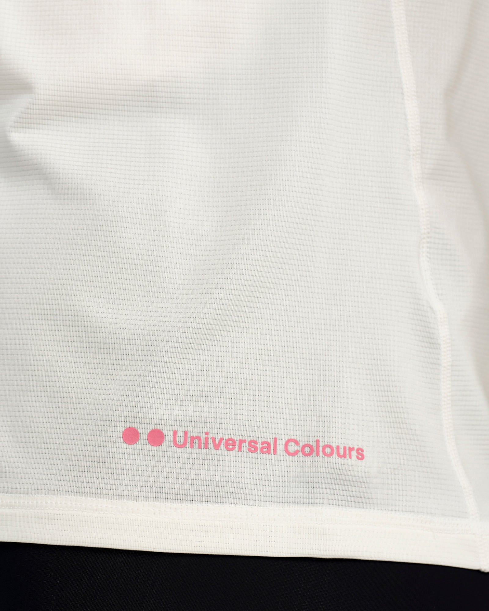 Hem detail close-up: pink Universal Colours wordmark on the Off White Long Sleeve Tech Tee, with visible textured weave.