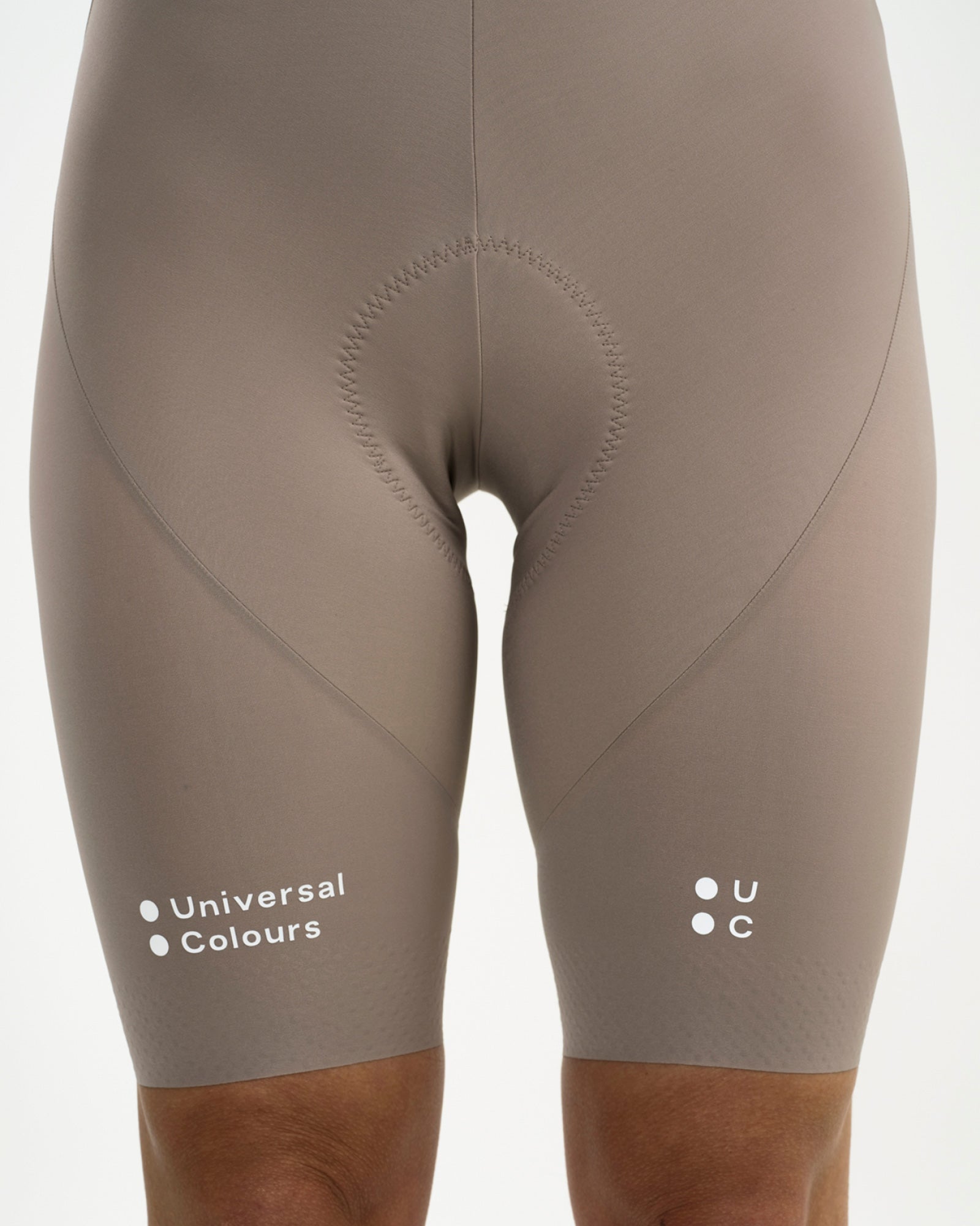 Close-up of the Women's Chroma Bib Short in Moon Grey: tonal Universal Colours wordmark and UC dot mark on the leg hems.