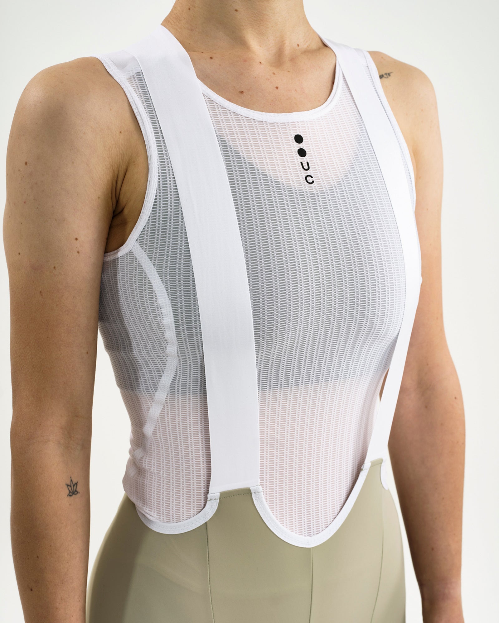 Front close-up of the white crossover bib straps over a Universal Colours mesh base layer with chest UC dots logo.