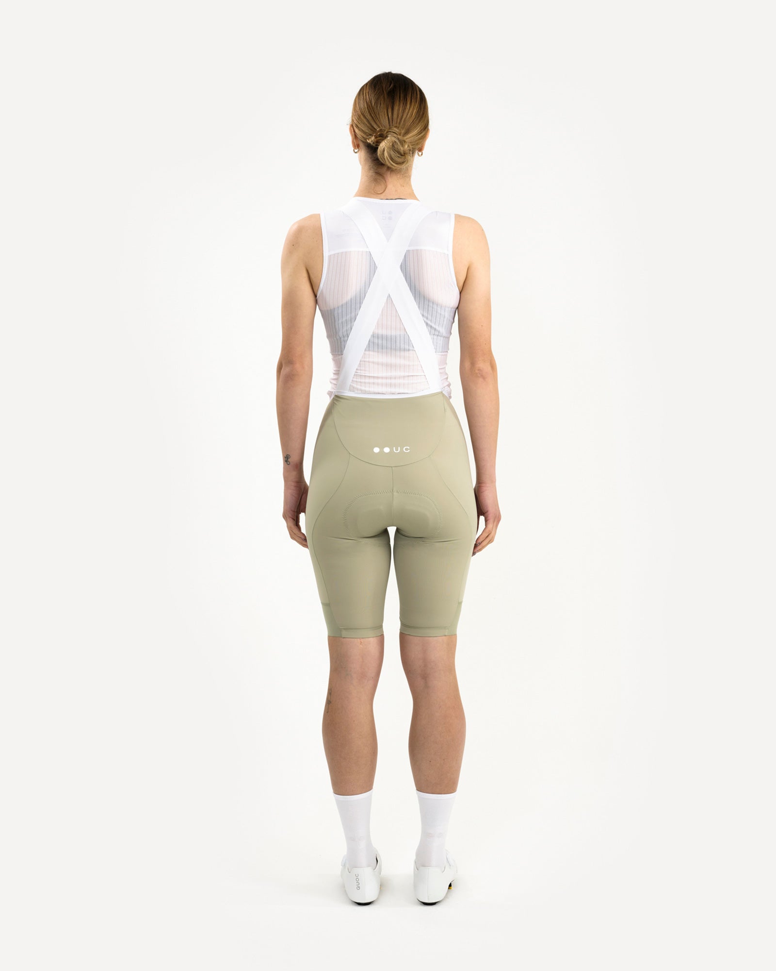 Back view: model wearing the Women's Mono Bib Shorts 2.0 in Green Tea with white UC logo on the dropped rear yoke.