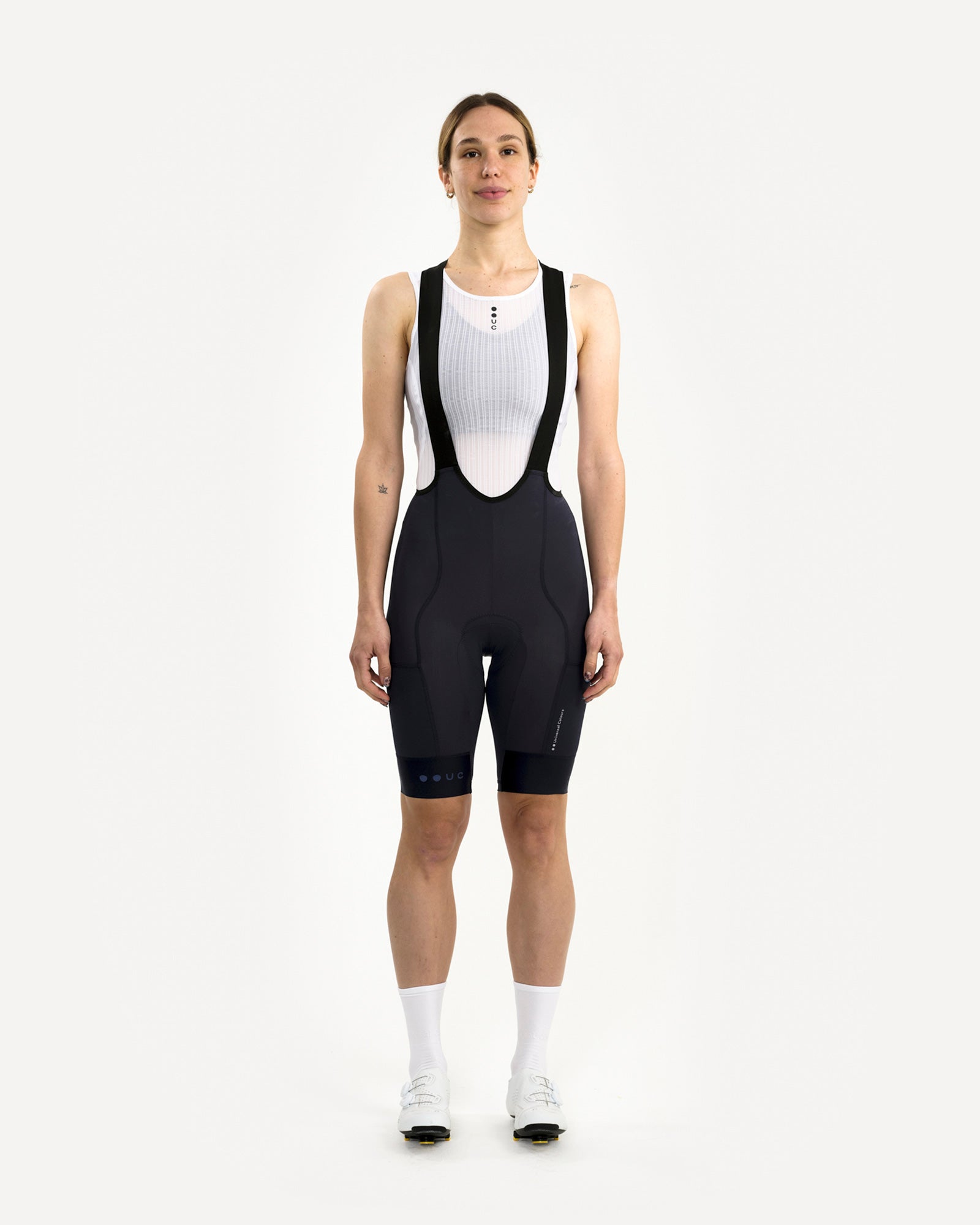Model wearing the Women's Mono Cargo Bib Short in Navy Blue, front view, styled with white UC mesh base layer.