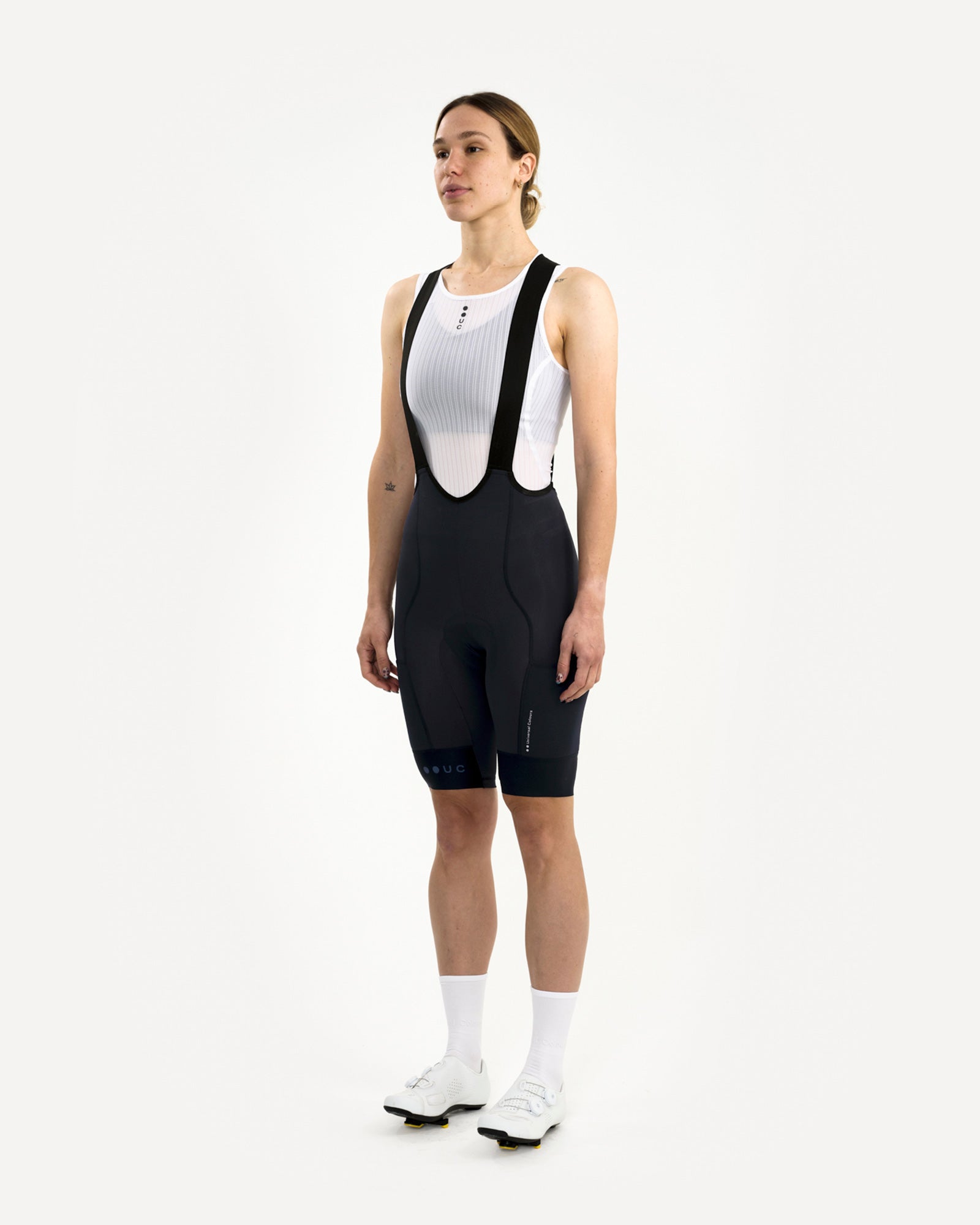 Front three-quarter view: model in the Women's Mono Cargo Bib Short in Navy Blue with white UC mesh base layer.