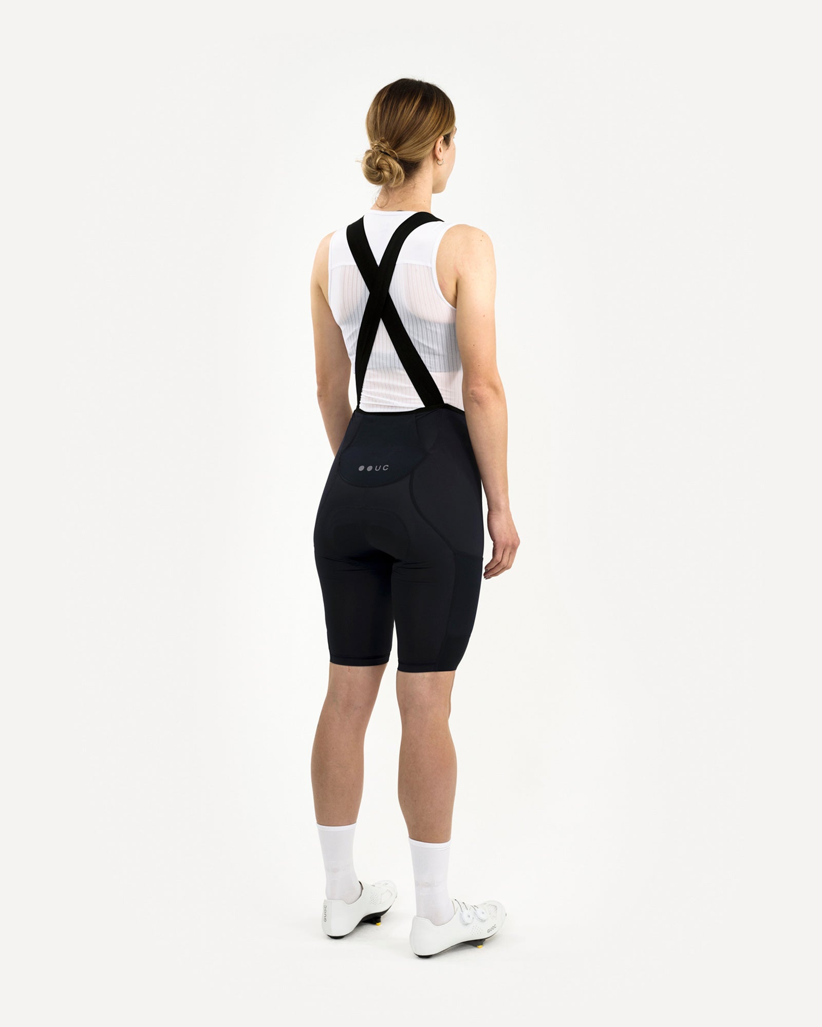 Back view: model in the Women's Mono Cargo Bib Short in Navy Blue, showing the black X-cross bib straps.