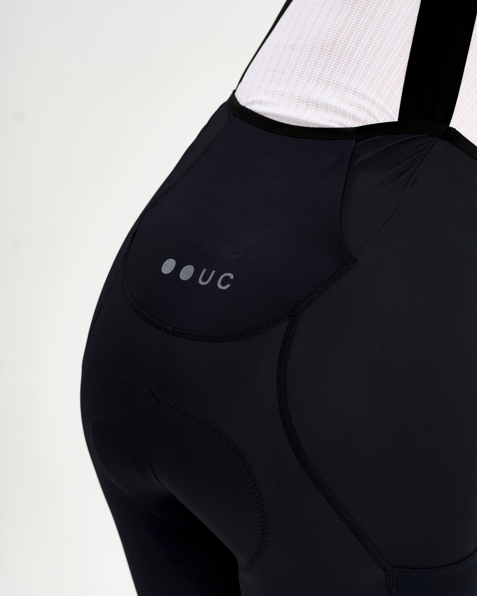 Rear yoke detail: tonal UC dot logo on the upper back panel of the Women's Mono Cargo Bib Short in Navy Blue.