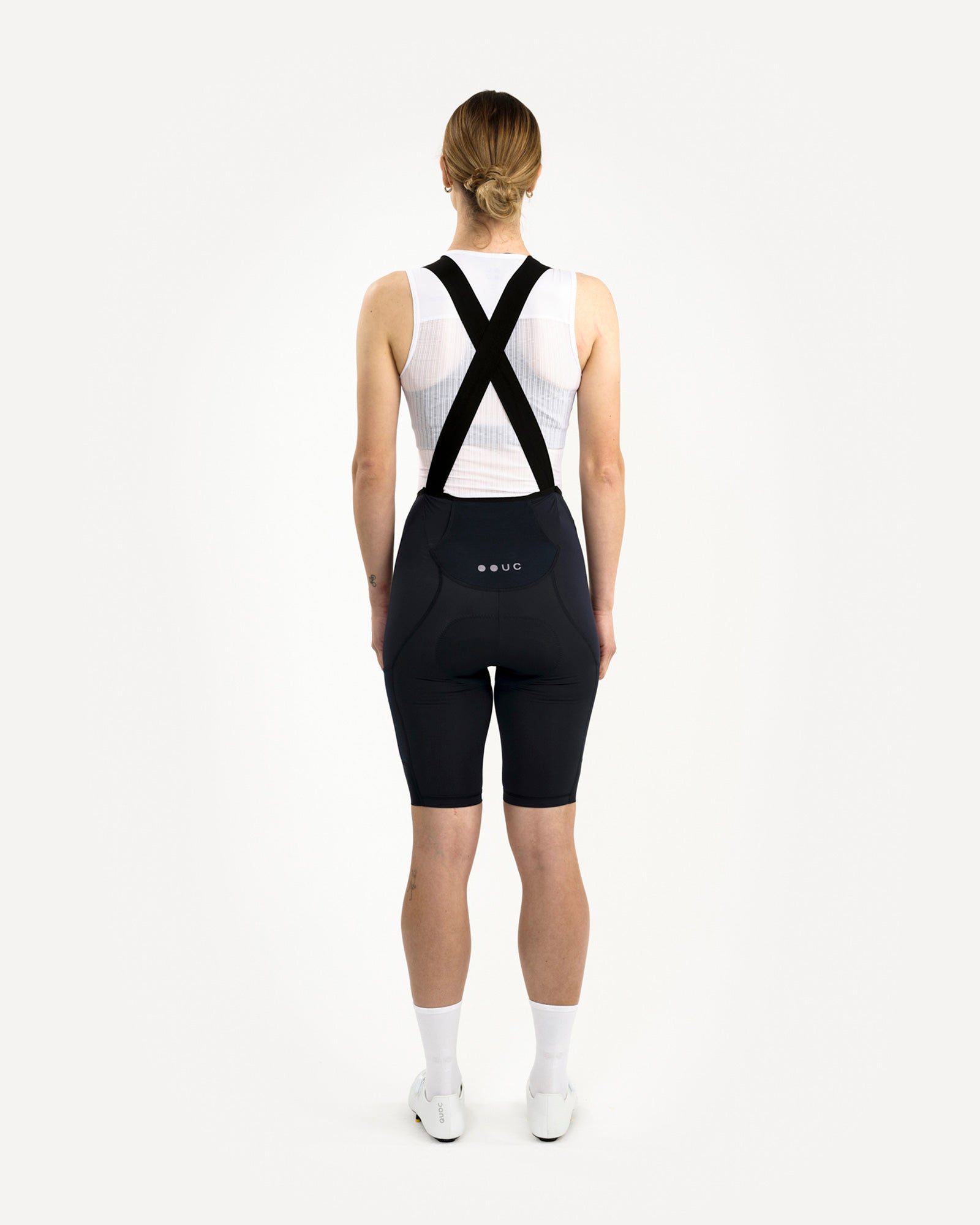Rear view of the model in the Women's Mono Cargo Bib Short in Navy Blue with black X-cross bib straps and dropped yoke.