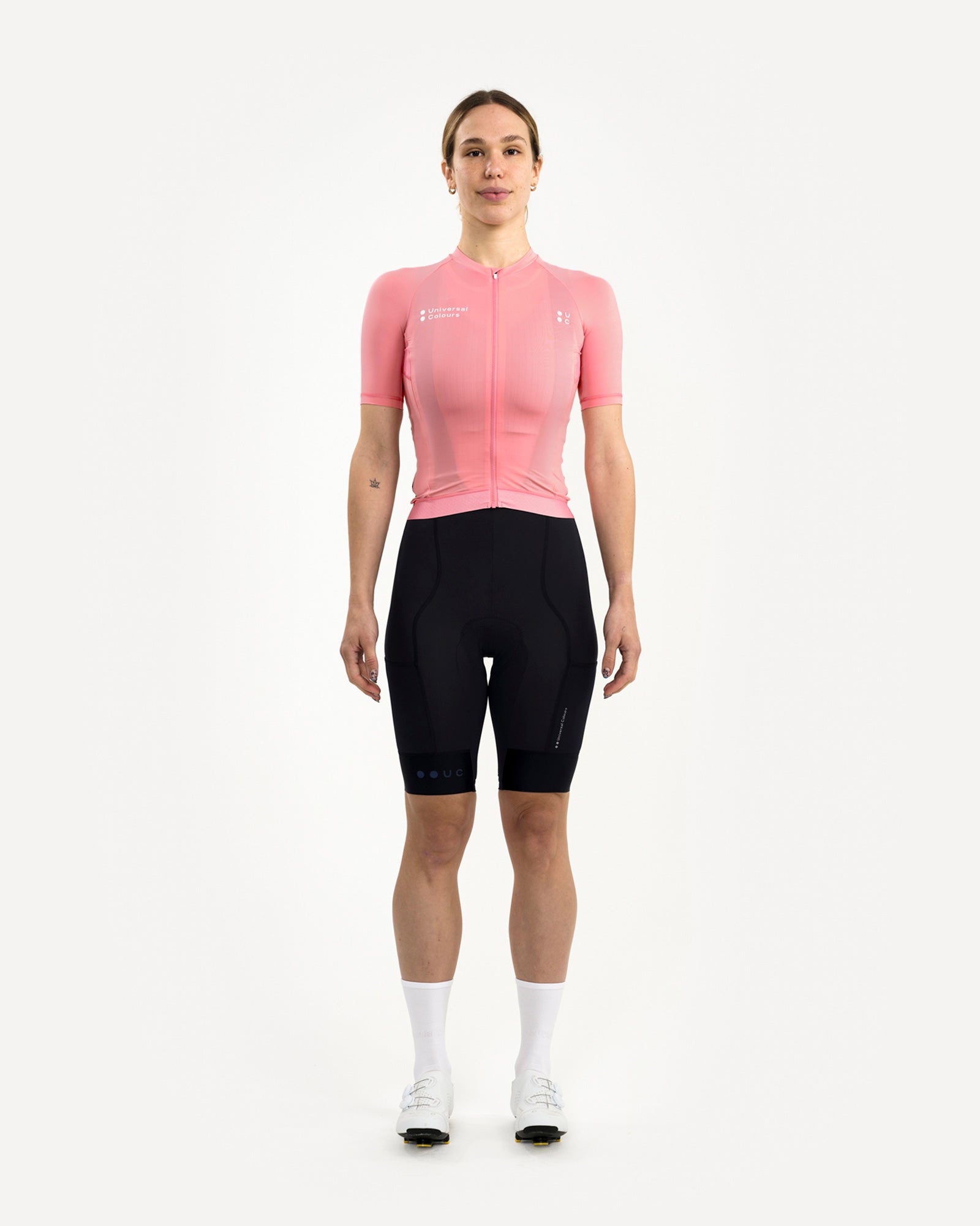 Front view: model wearing the Women's Mono Short Sleeve Jersey in Pink with black bib shorts, white socks and shoes.