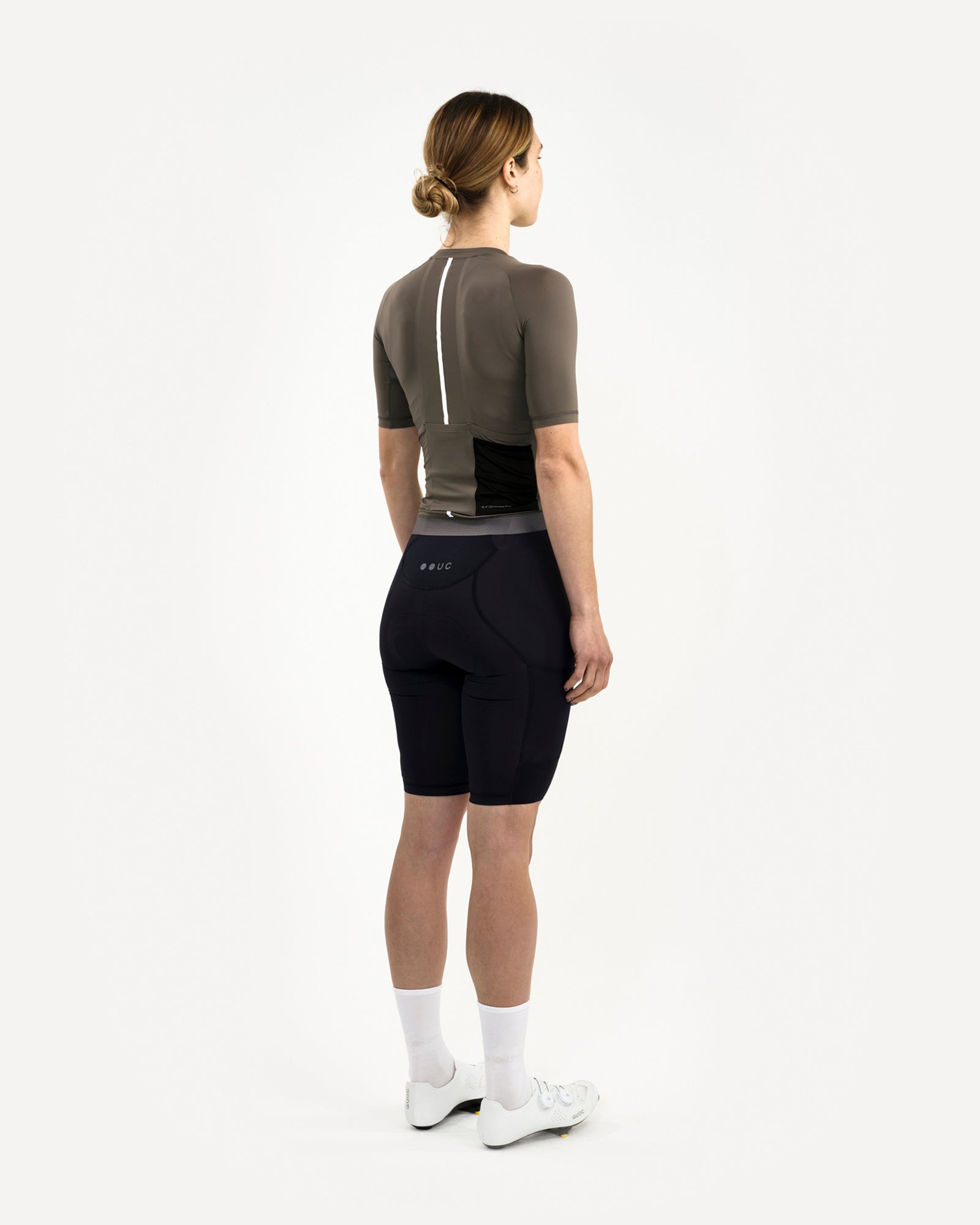 Rear three-quarter view: Women's Mono Short Sleeve Jersey in Soft Grey, styled with black UC bib shorts and white shoes.