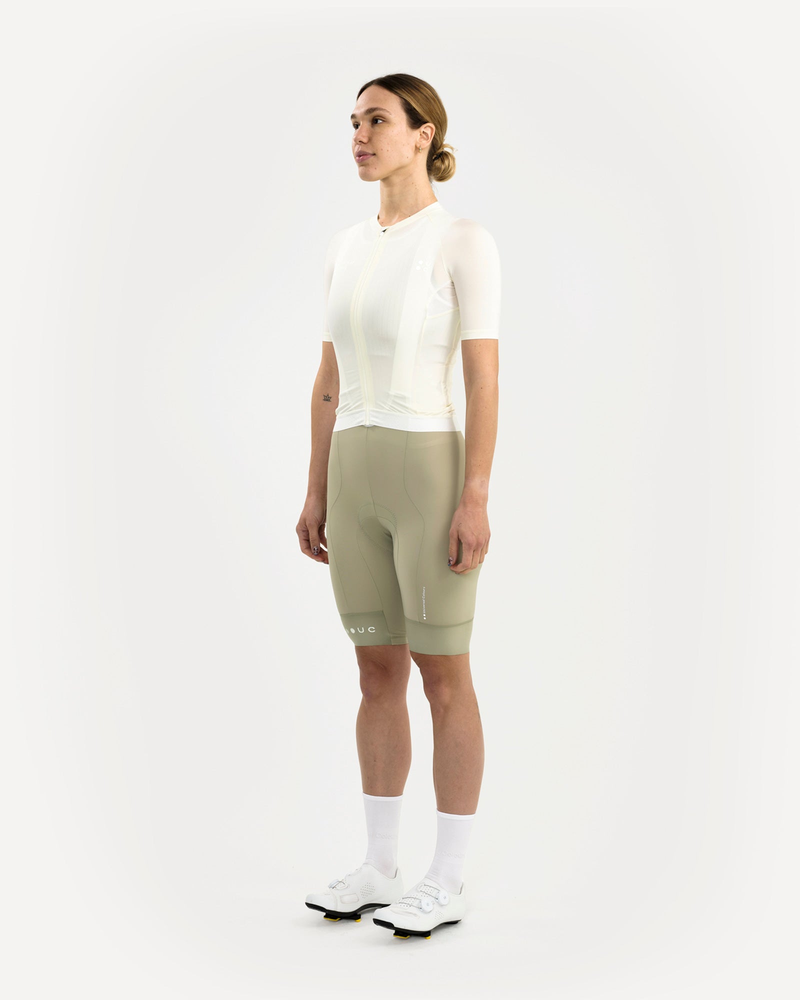 Model front three-quarter view in the Women's Mono Short Sleeve Jersey, Tampered White, paired with sage bib shorts.