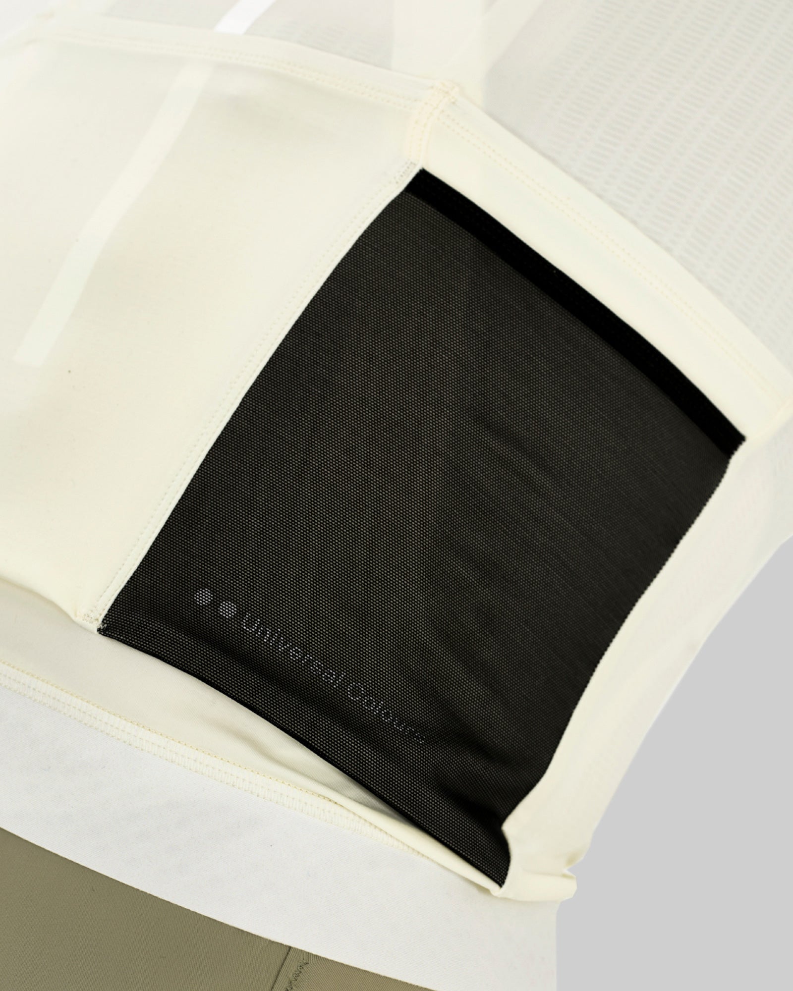 Rear pocket detail: black mesh stash pocket with tonal Universal Colours wordmark, set into the Tampered White jersey back.