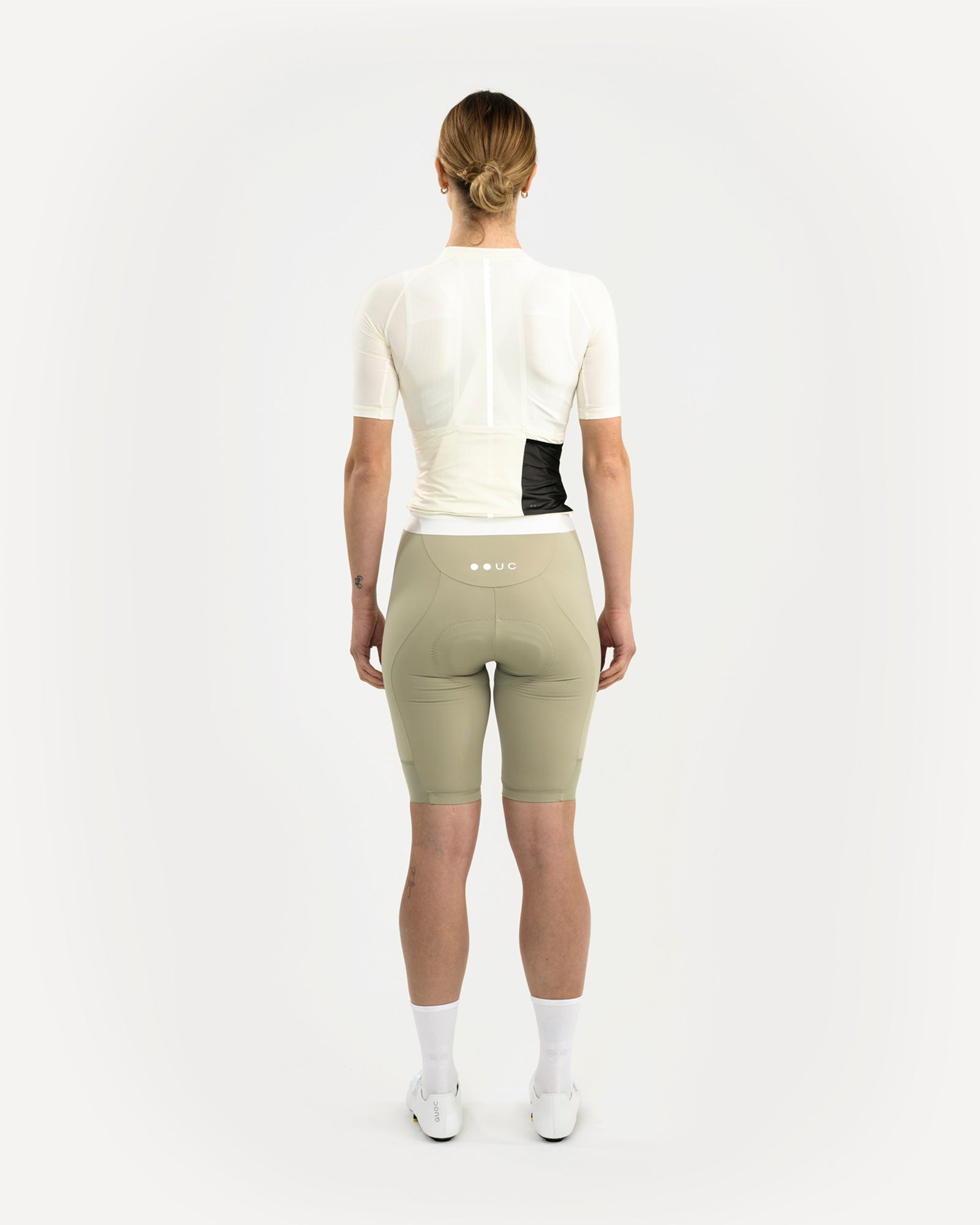 Back view: model wears the Tampered White Mono jersey with sage bib shorts; rear pockets show through translucent fabric.