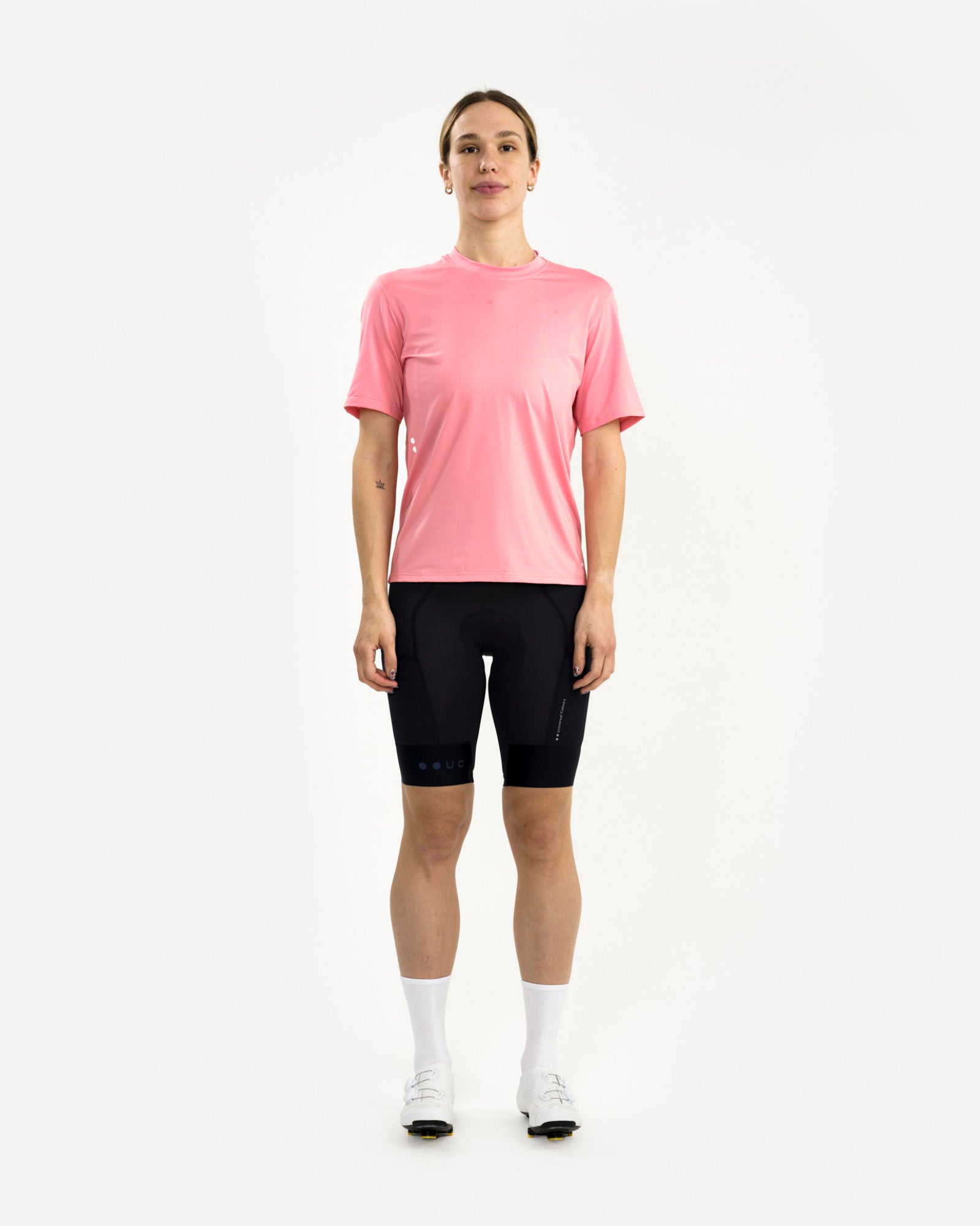 Female model front view in the Tech Tee in Washed Pink with black UC bib shorts, white socks and cycling shoes.