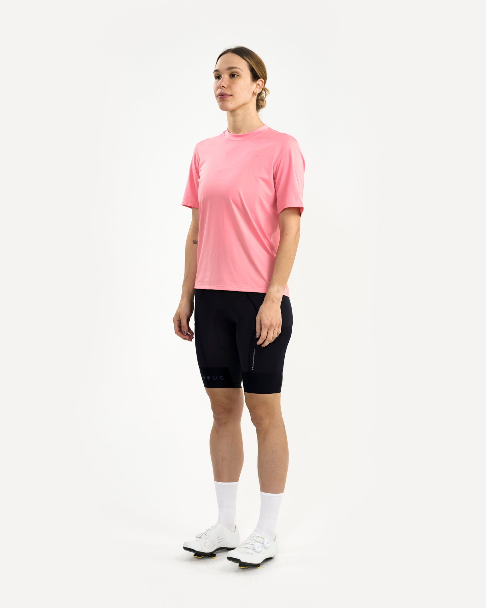 Three-quarter front view of a female model in the Tech Tee in Washed Pink and black UC cycling bib shorts.