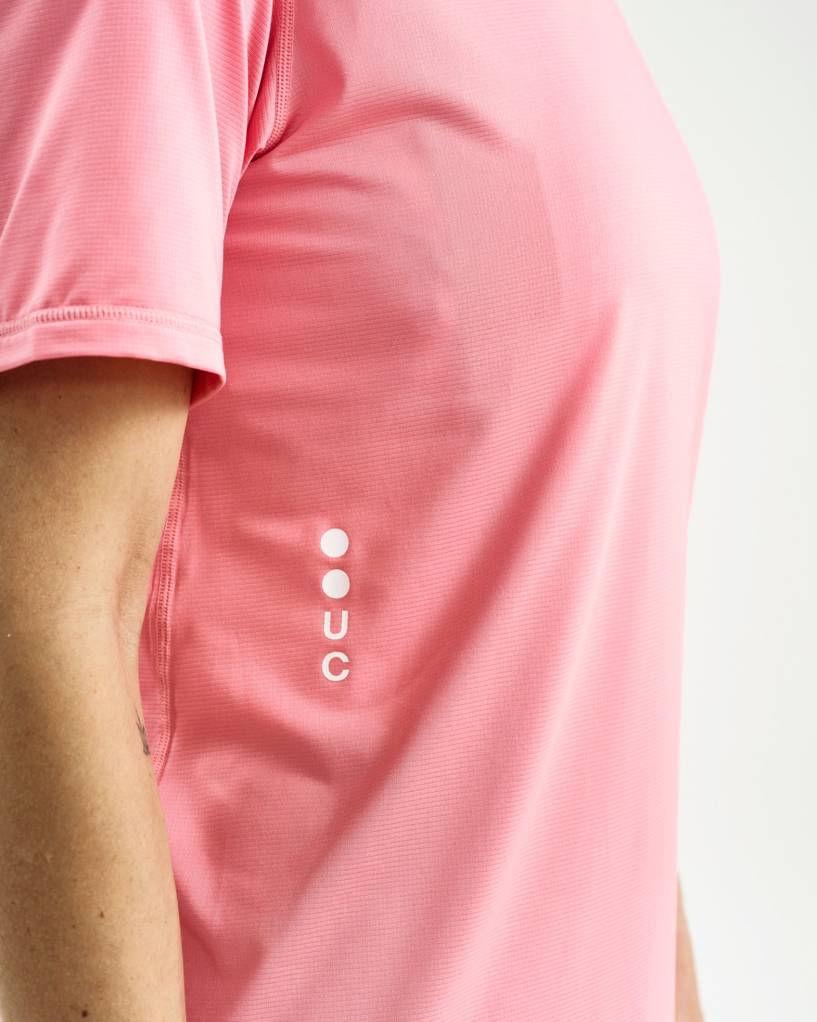 Side detail: white vertical UC dot-logo on the Tech Tee in Washed Pink, against the textured ribbed mesh fabric.