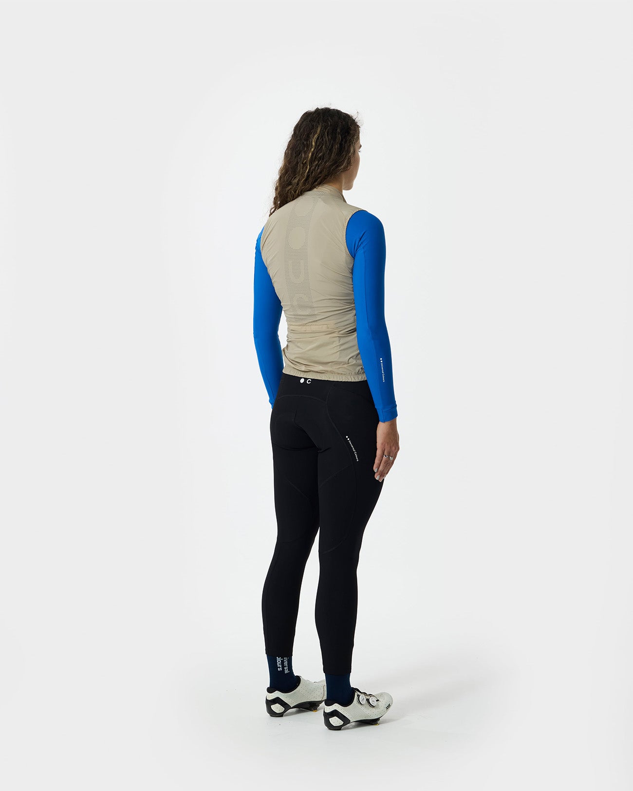 Back view: Women's Mono Gilet 2.0 in Rice Beige with perforated UC back panel, over a cobalt base layer and black bibs.