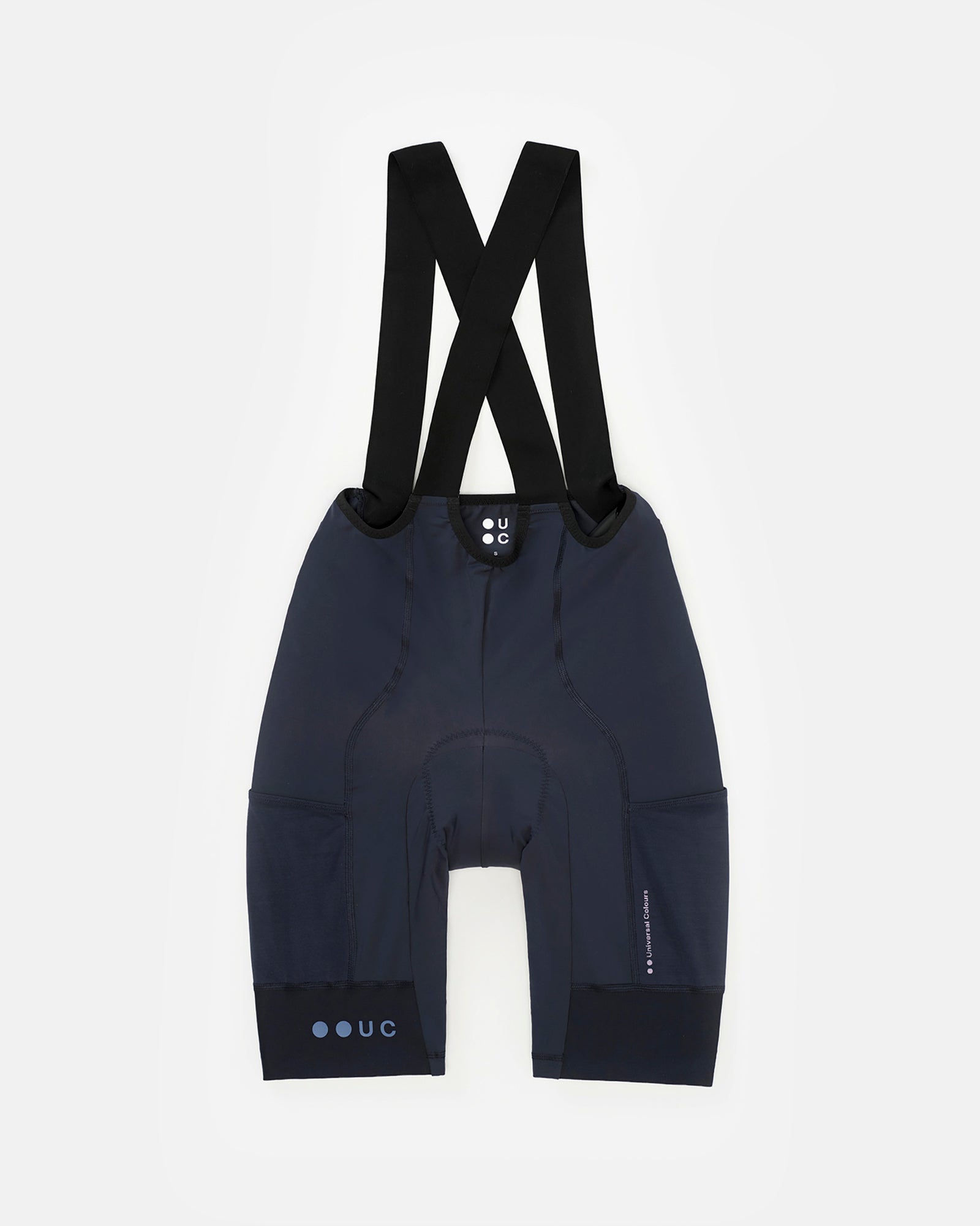 Flatlay rear view: Women's Mono Cargo Bib Short in Navy Blue with black X-cross bib straps and tonal UC leg-cuff logo.