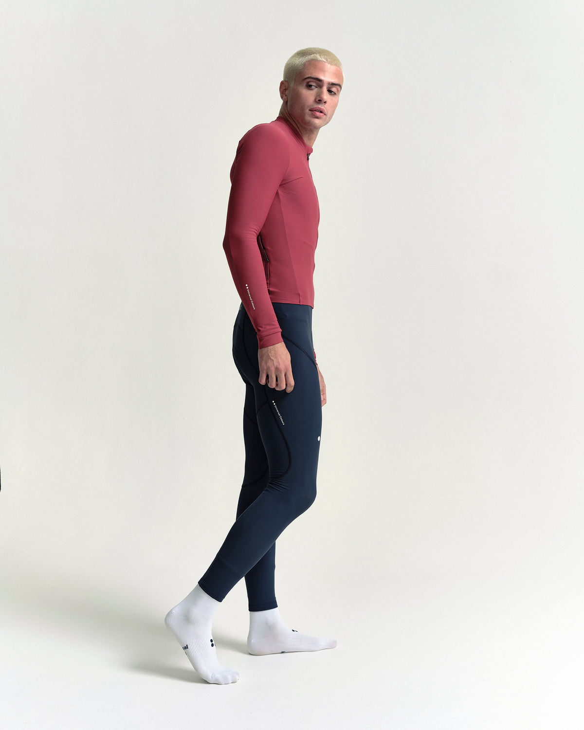 Model walking in the Men's Mono Long Sleeve Jersey in Apple Red, full-length view.