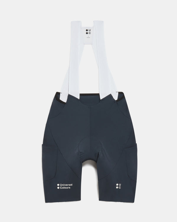 Flatlay of the Women's Chroma Cargo Bib Shorts in Navy Blue: ribbed bib straps, a pocket on each thigh and Universal Colours leg logos.