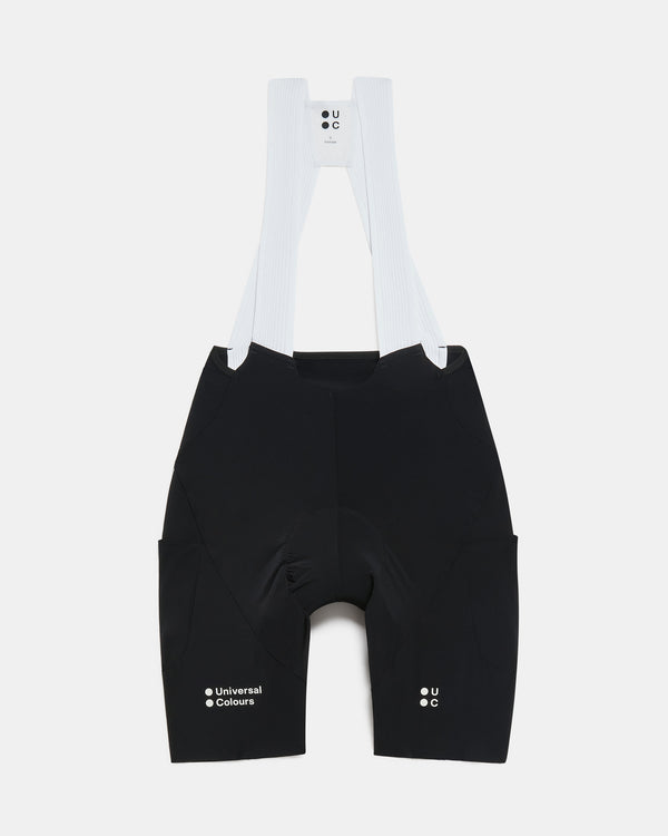 Flatlay of the Women's Chroma Cargo Bib Shorts in Black: ribbed bib straps, a pocket on each thigh and Universal Colours leg logos.