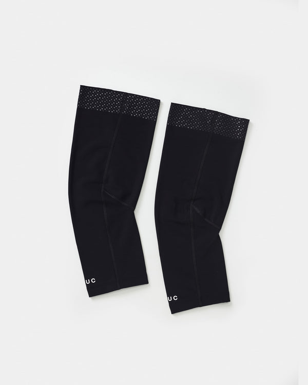 Flatlay of the Universal Colours Knee Warmers in Black, pair laid side by side showing silicone grip dot band at the thigh.
