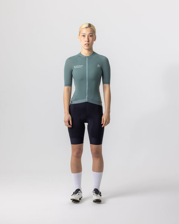 Model wearing the Women’s Mono Short Sleeve Jersey in Green Daze, paired with black UC bib shorts and white UC socks.