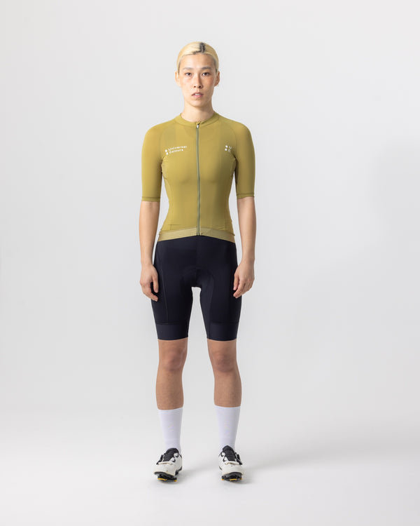 Model wearing the Women's Mono Short Sleeve Jersey in Olive Gold, paired with black UC bib shorts and white UC socks.