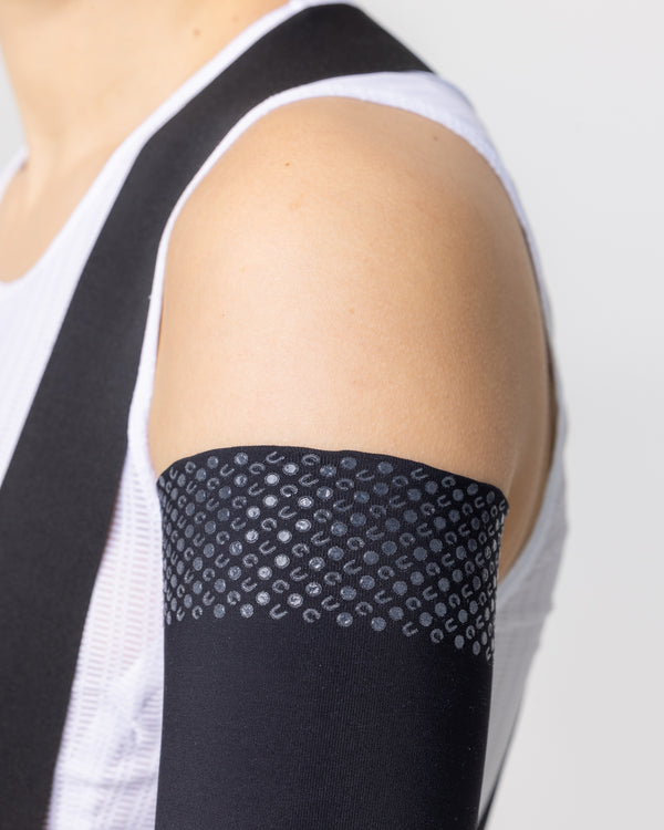Close-up of the silicone UC-motif gripper band on the Black Arm Warmer, worn over the bicep with white base layer.