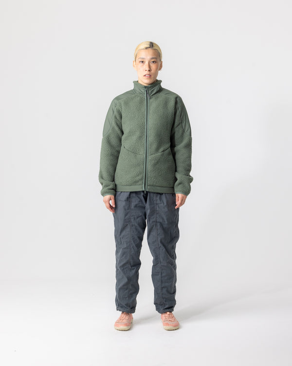 Front view: woman wearing the Unisex Fleece Jacket in Green zipped up, paired with charcoal ripstop trousers.