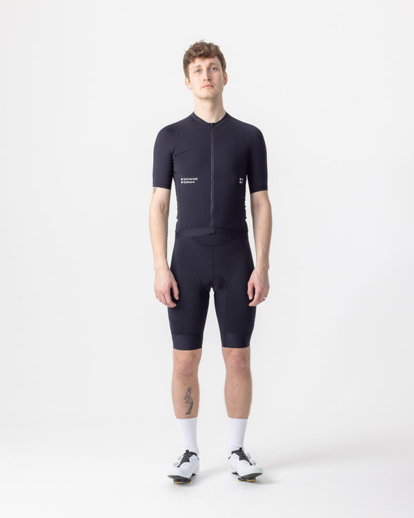 Model wearing the Men's Mono Short Sleeve Jersey in Black, front view, paired with black cycling bib shorts.