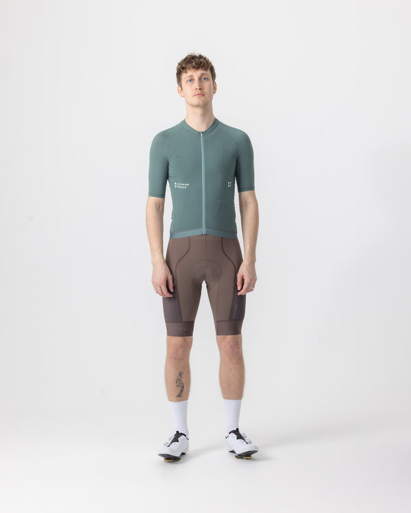 Model wearing the Men's Mono Short Sleeve Jersey in Green Daze, front view, paired with mosswood brown bib shorts.