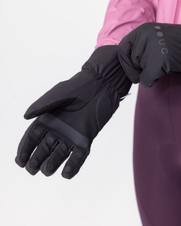Model wearing the Deep Winter Gloves in Black with a pink rain jacket and aubergine bib tights, hands clasped at the waist.