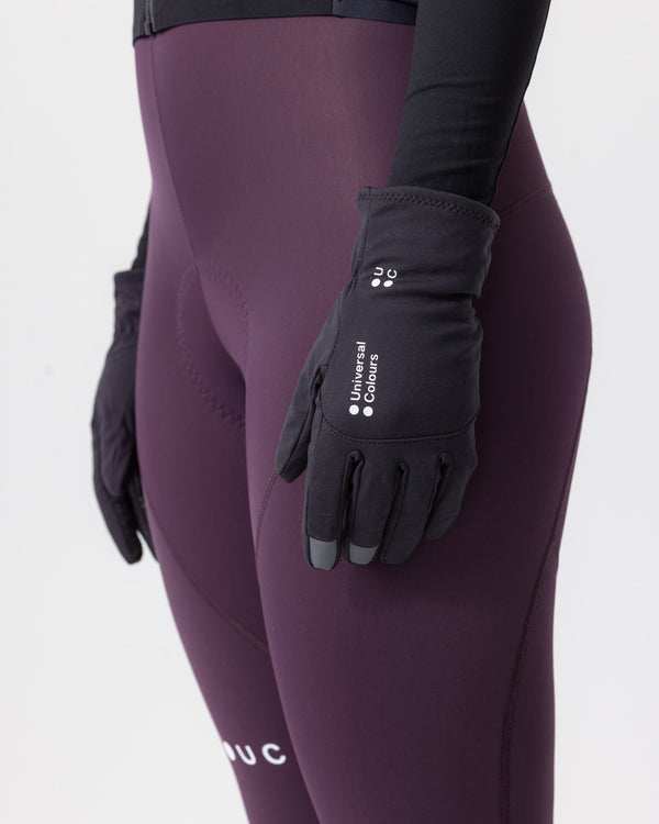 Model wearing the Mono Thermal Gloves in Black with aubergine bib tights, back-of-hand view with touchscreen fingertips.