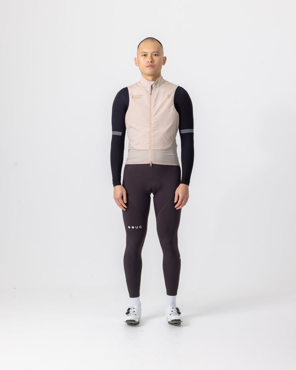 Male model wearing the Unisex Chroma Insulated Gilet in Almond Beige over a black base layer and brown bib tights.