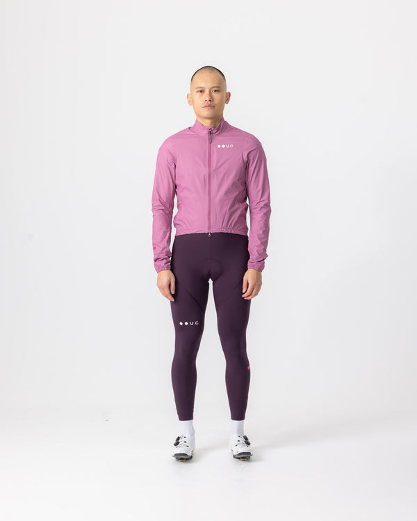 Model wearing the Men's Mono Rain Jacket in Soft Pink, front view, paired with aubergine cycling bib tights.