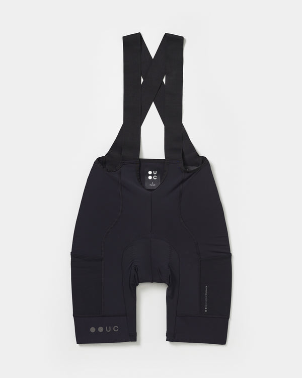 Women's Mono Cargo Bib Shorts in Black, front flatlay showing crossed straps, mesh side cargo pocket and UC hem mark.