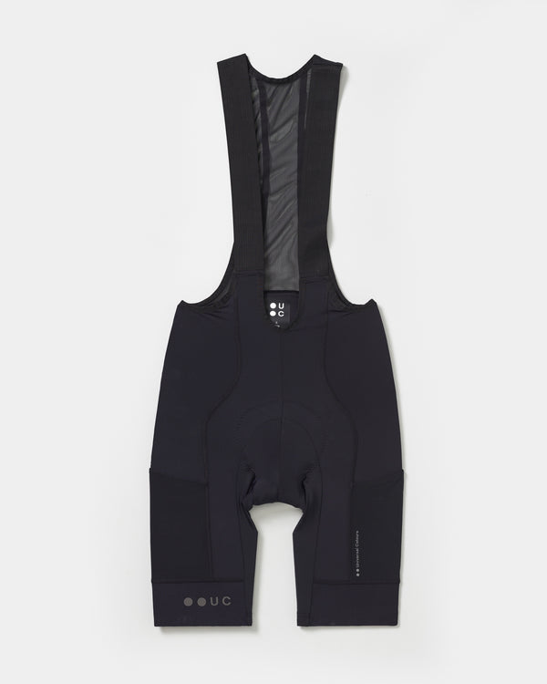 Flatlay: Men's Mono Cargo Bib Shorts in Black with black mesh bib straps and outer-thigh cargo pocket panels.