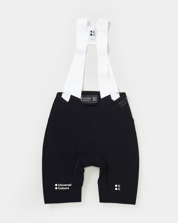Flatlay of the Chroma Women's Bib Short in Black, showing white ribbed bib straps and grippy textured leg cuffs.