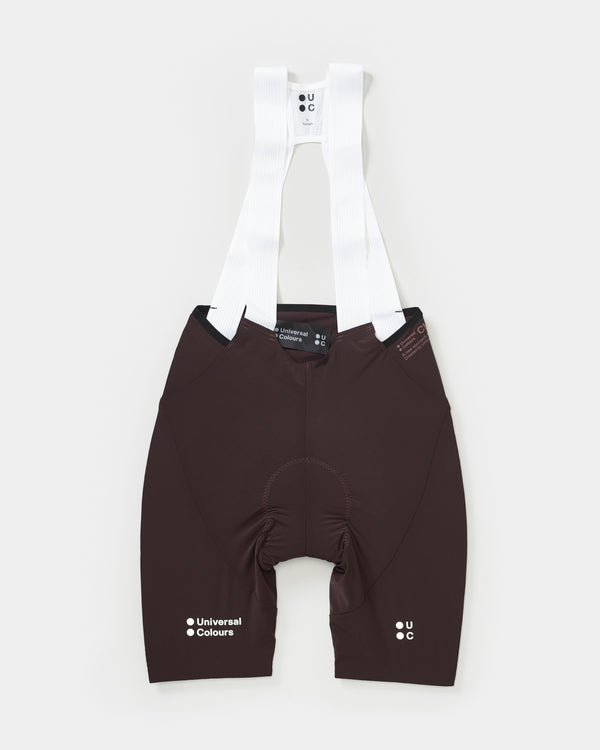 Flatlay: Women's Chroma Bib Shorts in Heavy Bark Brown with white ribbed mesh bib straps and tonal UC leg logos.