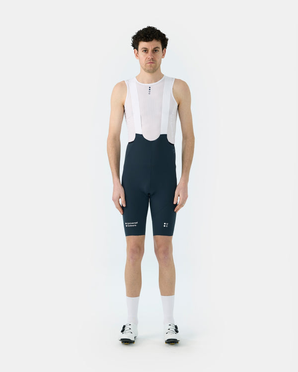 Model wearing the Men's Chroma Bib Short in Navy Blue with a white mesh base layer, white socks and road shoes.