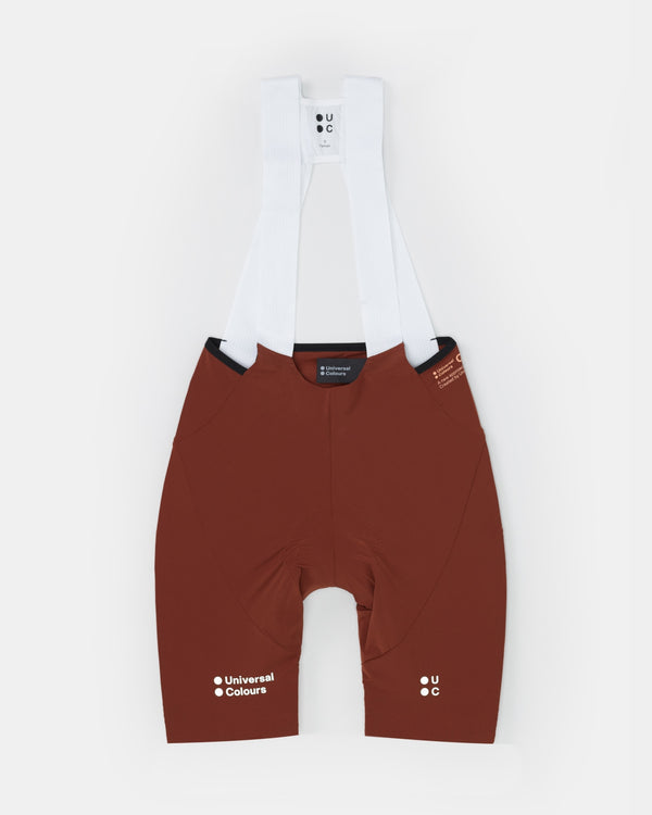Flatlay of the Women's Chroma Bib Shorts in Brick Red, with white mesh bib uppers and tonal UC waistband print.